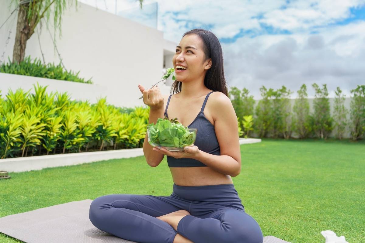Zdjęcie przedstawia kobietę w stroju sportowym, która je sałatkę