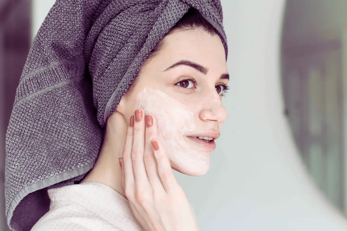 Kobieta aplikuje na skórę peeling enzymatyczny w kremie