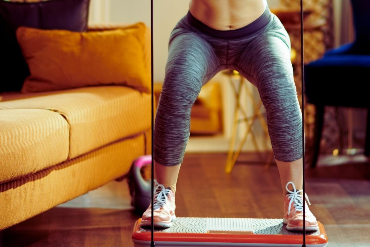 Kobieta wykonuje trening na platformie wibracyjnej z taśmami oporowymi